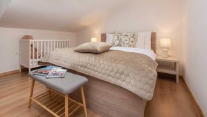 A bedroom with a bunk bed, a bedside table with a lamp, a small bench, and a crib with a teddy bear. - Seaview Family Villa With Heated Pool (Okrug)