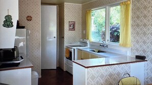 A compact kitchen with a refrigerator, stove, sink, and a window with yellow curtains. - A short walk to the beautiful Lake Taupo relax and take in the fabulous views! (Kuratau)