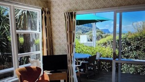 A room with a TV, a chair, a table, and a view of the outdoors. - A short walk to the beautiful Lake Taupo relax and take in the fabulous views! (Kuratau)