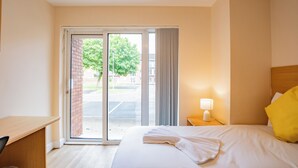A hotel room with a bed, a desk, a nightstand with a lamp, and a sliding glass door leading to an outdoor area. - Comfortable Limerick City Stay (Limerick)