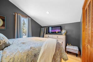 Ein Schlafzimmer mit einem Bett, einem Fernseher, einer Kommode und einem Fenster mit Vorhängen.