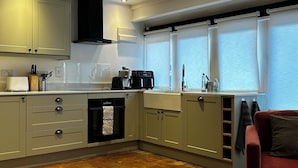 A modern kitchen with a dining area, including a wooden table and a red chair. - The Little House Annex – A Peaceful Countryside Stay in Beautiful Shotteswell. (Shotteswell)