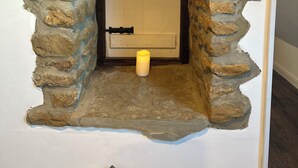 A stone-arched doorway leading to a room with a white door, a candle on the floor, and a wooden beam above. - The Little House Annex – A Peaceful Countryside Stay in Beautiful Shotteswell. (Shotteswell)