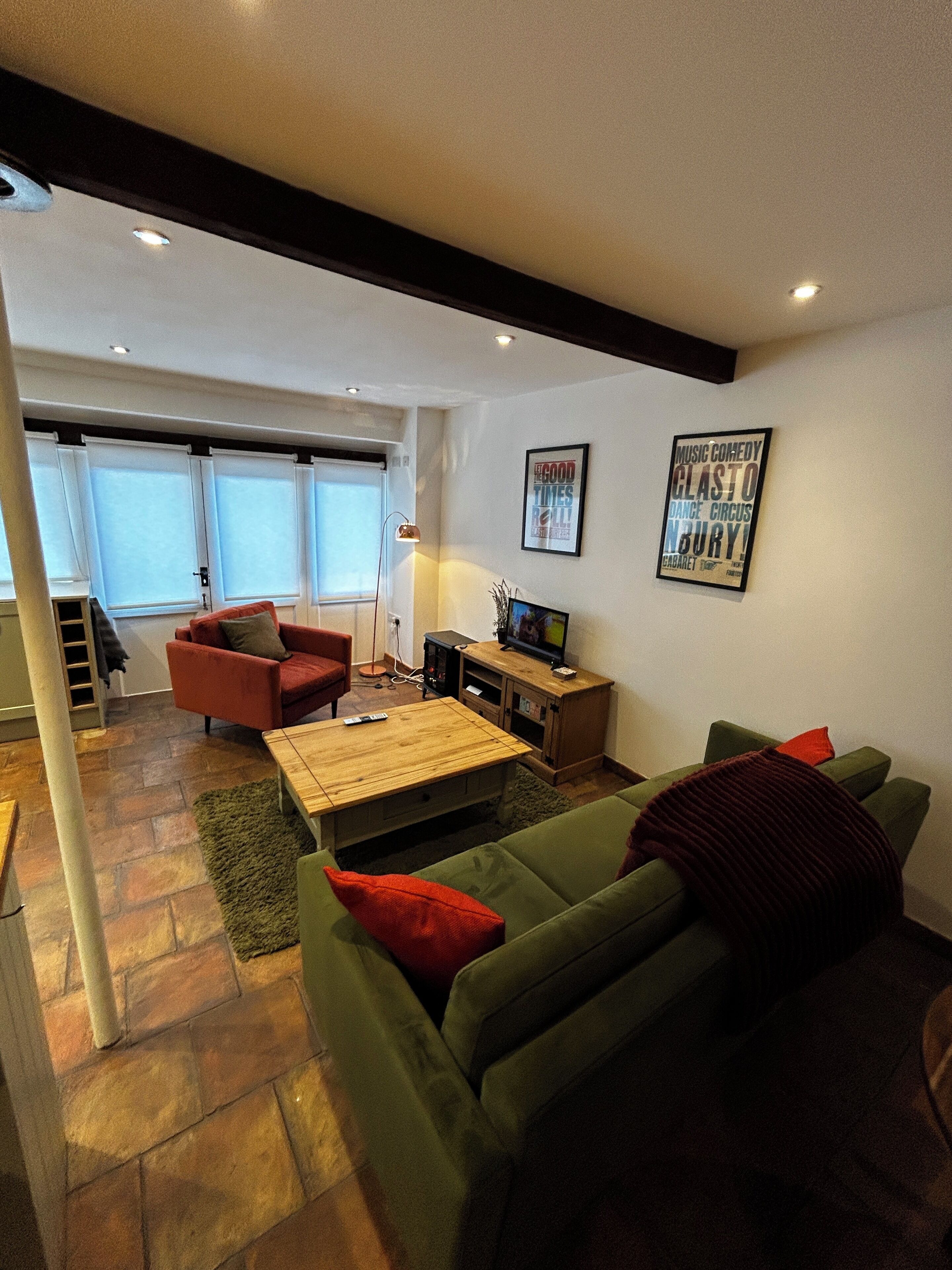 Een woonkamer met een groene bank, een rode fauteuil, een houten salontafel en een televisie op een houten dressoir.
