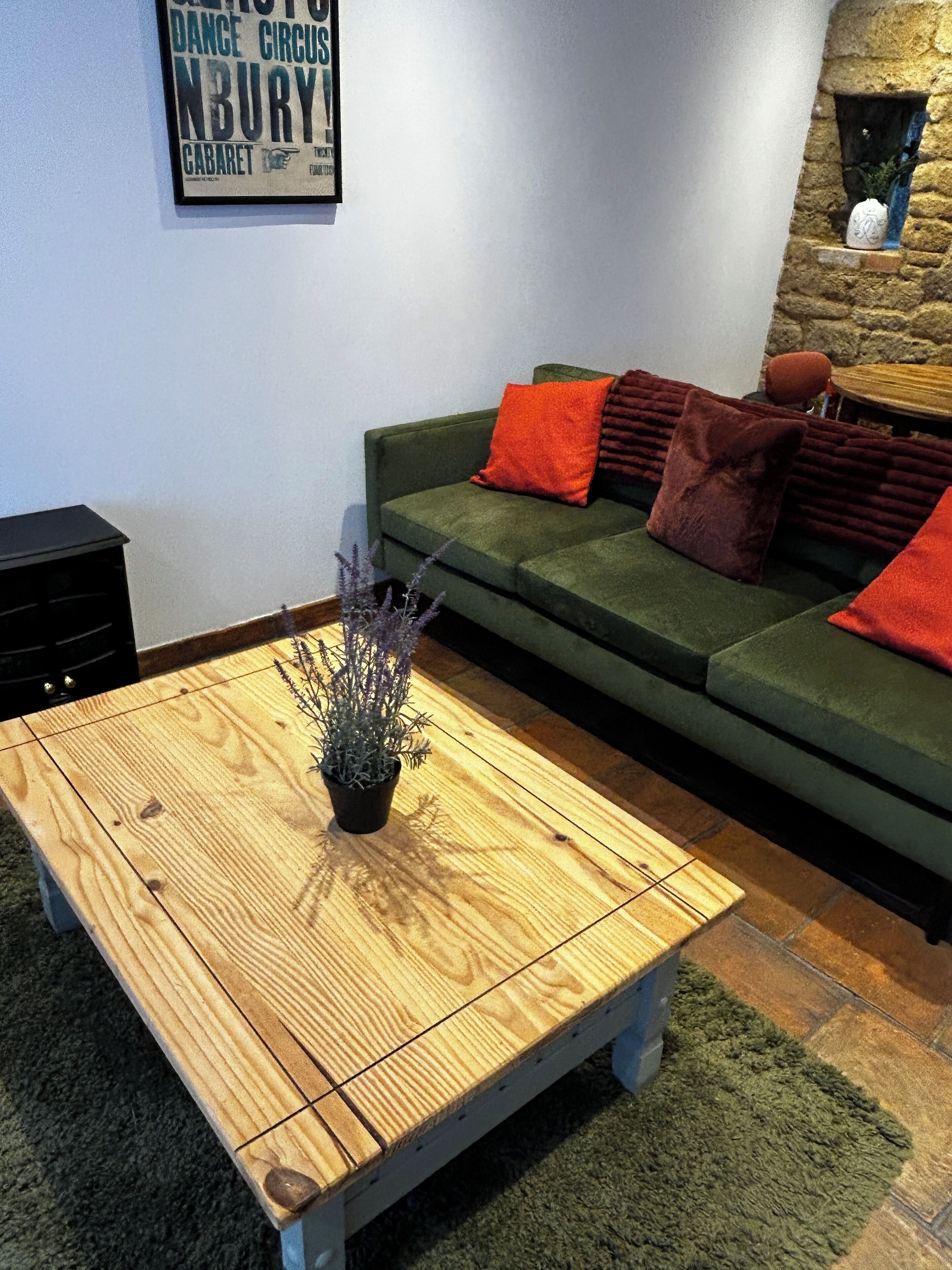 A living room with a green sofa, a wooden coffee table with a plant, and a stone fireplace.