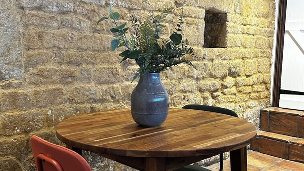 A round wooden table with a blue vase, two chairs, and a stone wall. - The Little House Annex – A Peaceful Countryside Stay in Beautiful Shotteswell. (Shotteswell)