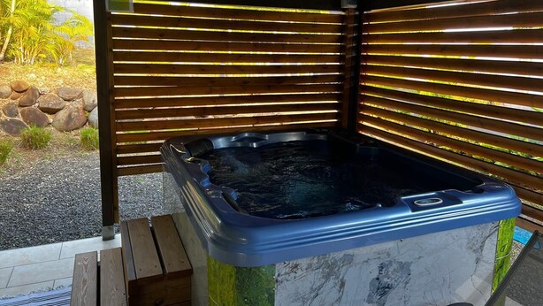 Een hottub onder een houten constructie, met uitzicht op rotsen en begroeiing.