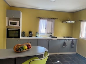 A compact kitchen with a microwave, stove, and sink. There is a fruit bowl on the counter and a chair. - LAKAZ'DELAIR - Quiet bungalow with Jacuzzi, close to town and beaches. (Sainte-Anne)