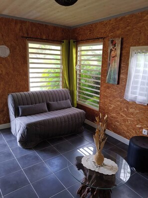 Una habitación con un sofá gris, una mesa de centro de cristal y un cuadro en la pared.