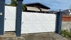 Een hekpoort met een witte garagepoort, een overdekt terras en een stenen muur.