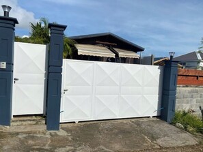 A gated entrance with a white garage door, a covered patio, and a stone wall. - LAKAZ'DELAIR - Quiet bungalow with Jacuzzi, close to town and beaches. (Sainte-Anne)