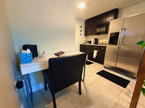 Cocina compacta con armarios oscuros, refrigerador de acero inoxidable y comedor con una silla negra.