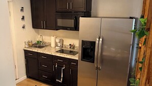 A modern kitchen with dark cabinets, a stainless steel refrigerator, a microwave, and a coffee maker. - Sunny Baldwin Park Studio • Walk to Cafés • Near Downtown (Orlando)