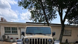 A beige Jeep with large off-road tires parked in front of a house. - Sunny Baldwin Park Studio • Walk to Cafés • Near Downtown (Orlando)