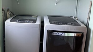 Two front-loading washing machines in a laundry room with shelves above for towels. - Sunny Baldwin Park Studio • Walk to Cafés • Near Downtown (Orlando)