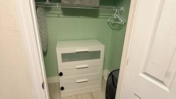A small walk-in closet with a white storage unit, a grey mat, and a hanging rack.
