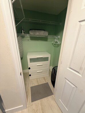 A small walk-in closet with a white storage unit, a grey mat, and a hanging rack.