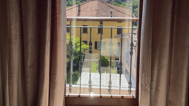 Un balcon avec vue sur un lac, des montagnes et un bâtiment jaune.