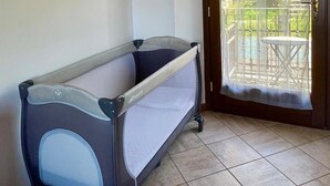 Une chambre avec un berceau, une porte-fenêtre coulissante donnant sur un espace extérieur équipé d’une table et de chaises, et un sol carrelé.