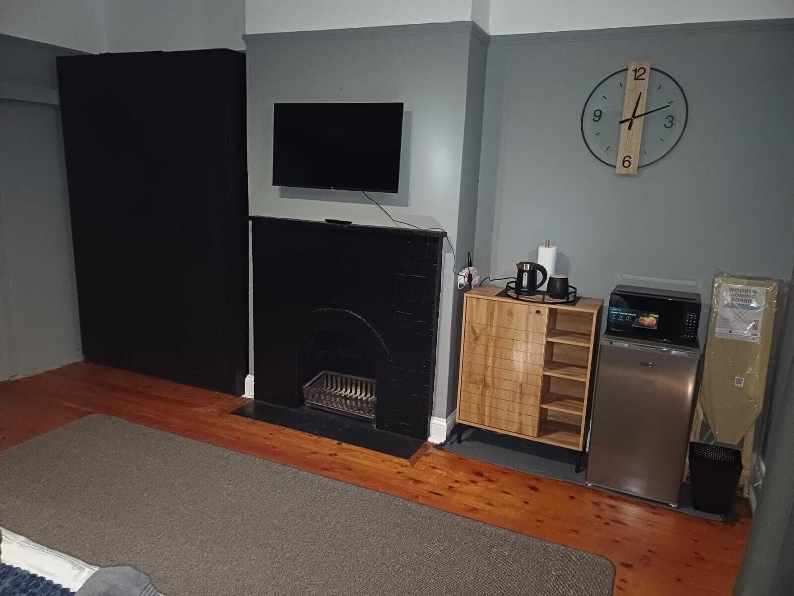 Una habitación con chimenea, televisor montado en la pared, un reloj y un refrigerador.