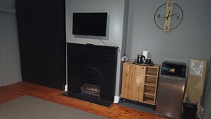 Una habitación con chimenea, televisor montado en la pared, un reloj y un refrigerador.
