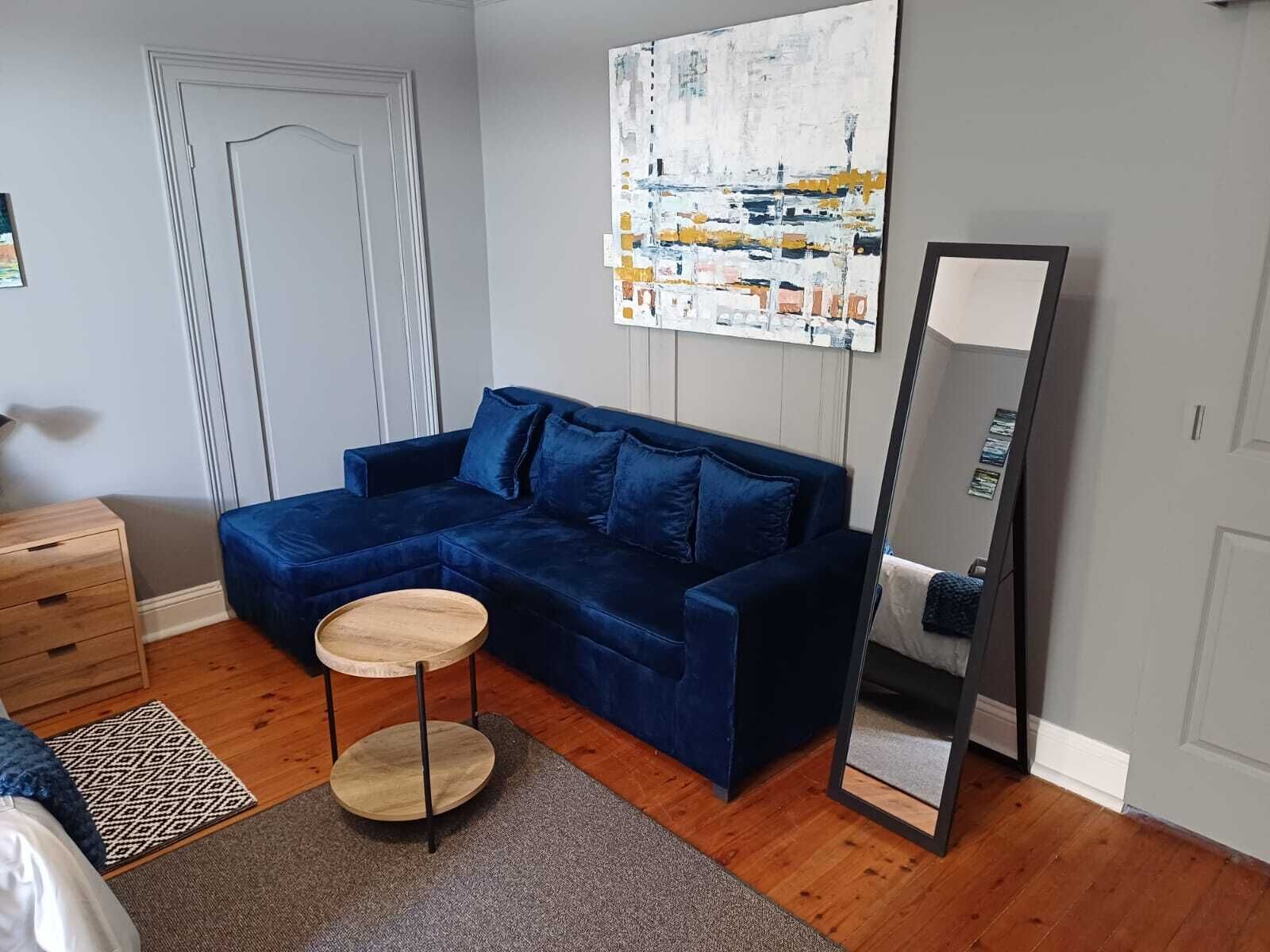 A room with a blue sofa, a round wooden table, a mirror, a dresser, and a patterned rug.