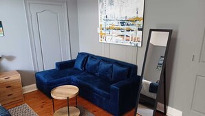 Una habitación con un sofá azul, una mesa redonda de madera, un espejo, un aparador y una alfombra estampada.