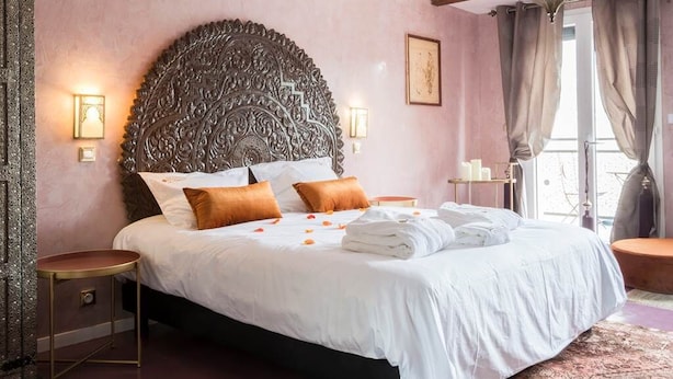 Une chambre à coucher avec une grande tête de lit décorée, un lit recouvert de draps blancs et une table de chevet avec une lampe.