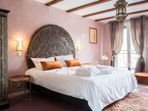Ein Schlafzimmer mit einem großen, verzierten Kopfteil, einem Bett mit weißen Leinentüchern und einem Nachttisch mit Lampe.