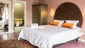 Une chambre à coucher avec un grand lit, une tête de lit en bois, une table de chevet et une salle de bain visible à travers une arche.