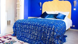 A bedroom with a blue and yellow color scheme, a bed with a blue sequin cover, and a decorative wall piece. - Majorelle room (Tours)