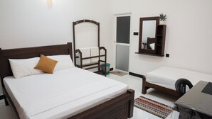 Um quarto com uma cama, uma cadeira, uma escrivaninha, um espelho e uma porta.