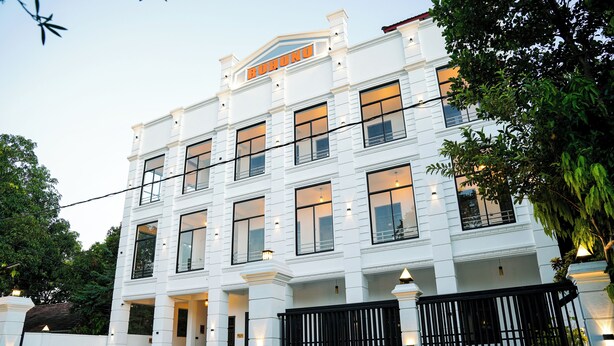 Um edifício de vários andares com fachada branca, grandes janelas e uma cerca de metal preta em frente.