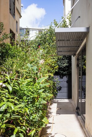 A narrow pathway flanked by dense foliage and a building with a metal awning. - Mamad Stay on Iconic Sheinkin St by SeaNRent (Tel-Aviv)