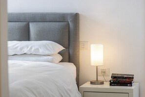 A neatly made bed with white linens and a grey headboard, a bedside lamp, and a stack of books on a nightstand. - Mamad Stay on Iconic Sheinkin St by SeaNRent (Tel-Aviv)