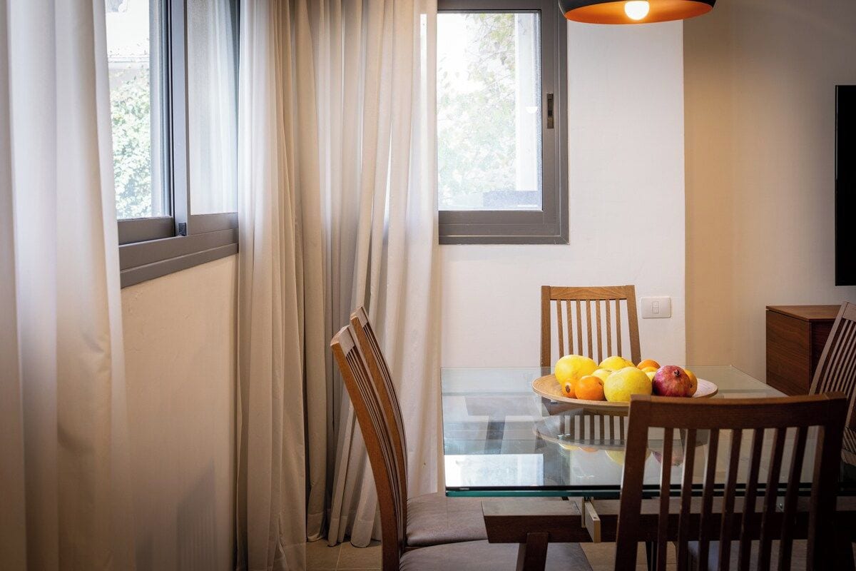 A dining area with a glass table, wooden chairs, and a fruit bowl.