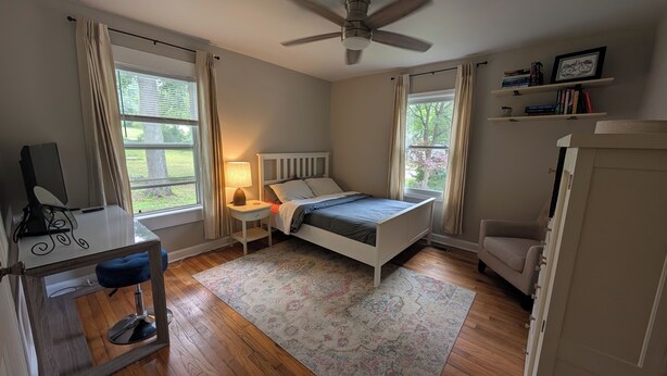 Ein Schlafzimmer mit Bett, Schreibtisch, Stuhl und Deckenventilator.