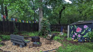 Ein Garten mit einer hölzernen Bank, einer Komposttonne und einem kleinen Tisch mit einem grünen Gegenstand darauf.