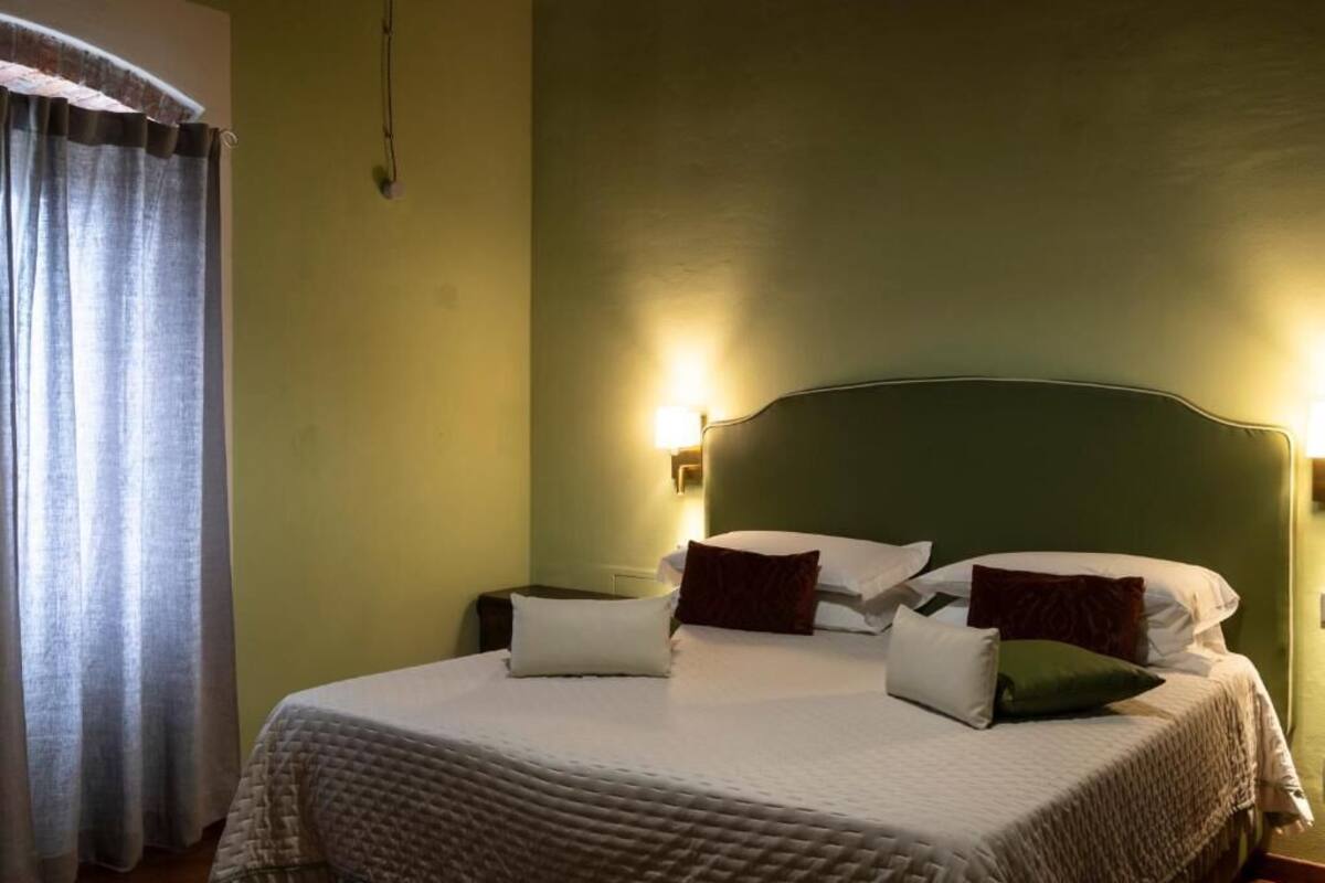 Una cama con cabecera, dos mesitas de noche y una lámpara de pared.
