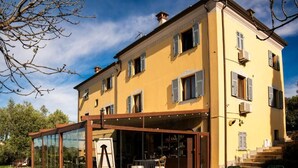A two-story building with a glass-enclosed patio area, a staircase leading to the upper floor, and a clear sky. - Locanda de Banchieri (Fosdinovo)