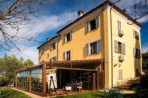 A two-story building with a glass-enclosed patio area, a staircase leading to the upper floor, and a clear sky. - Locanda de Banchieri (Fosdinovo)