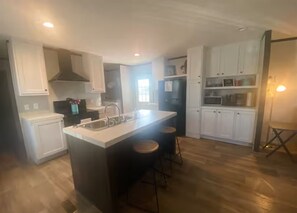 A kitchen with white cabinets, a central island with stools, and a refrigerator. - "Water View" Buck n Bass Camp (Florien)