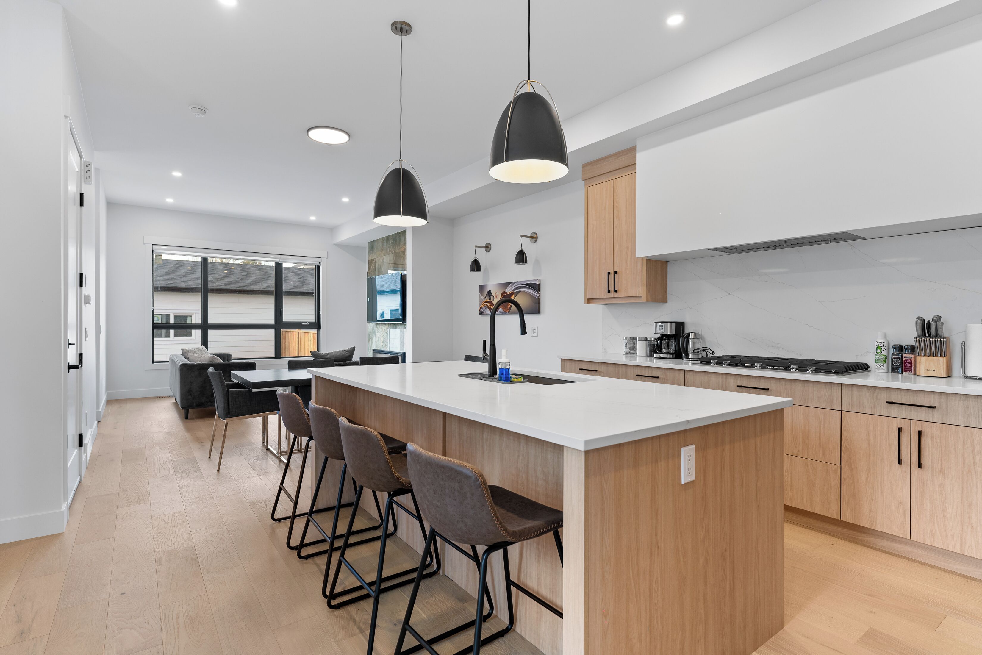 A modern kitchen with a large island, bar stools, pendant lighting, and a view to the living area.