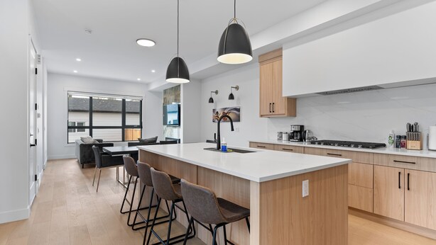 A modern kitchen with a large island, bar stools, pendant lighting, and a view to the living area. - Modern Luxury Home | 3 Min to University, Stadium & Major Hospitals (Calgary)