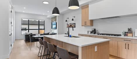 A modern kitchen with a large island, bar stools, pendant lighting, and a view to the living area.