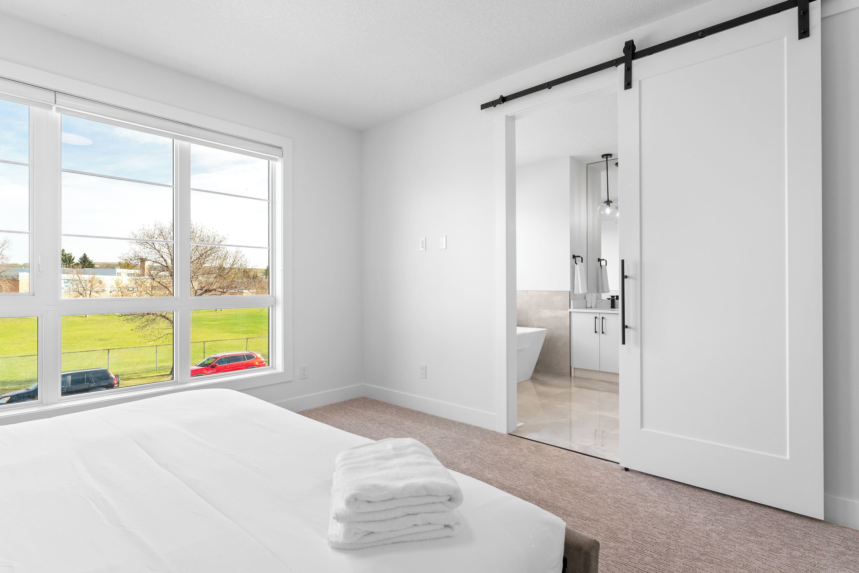 A bedroom with a bed, a window with a view, a sliding door to a bathroom, and a white color scheme.