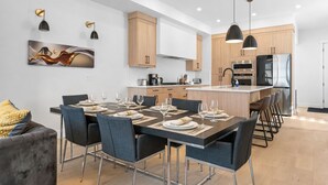 A modern kitchen with wooden cabinets, stainless steel appliances, and a dining area with a table set for four. - Modern Luxury Home | 3 Min to University, Stadium & Major Hospitals (Calgary)