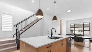 A modern kitchen with a central island, a built-in dishwasher, and pendant lighting. - Modern Luxury Home | 3 Min to University, Stadium & Major Hospitals (Calgary)