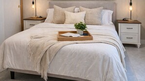 Une chambre à coucher comprenant un lit, des tables de chevet, un climatiseur, un luminaire fixé au mur et une plante placée sur la table de chevet.