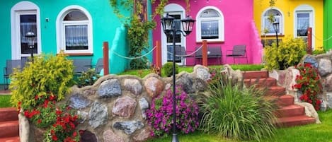 Un edificio colorido con un muro de piedra, una farola y un pequeño jardín con flores y plantas.